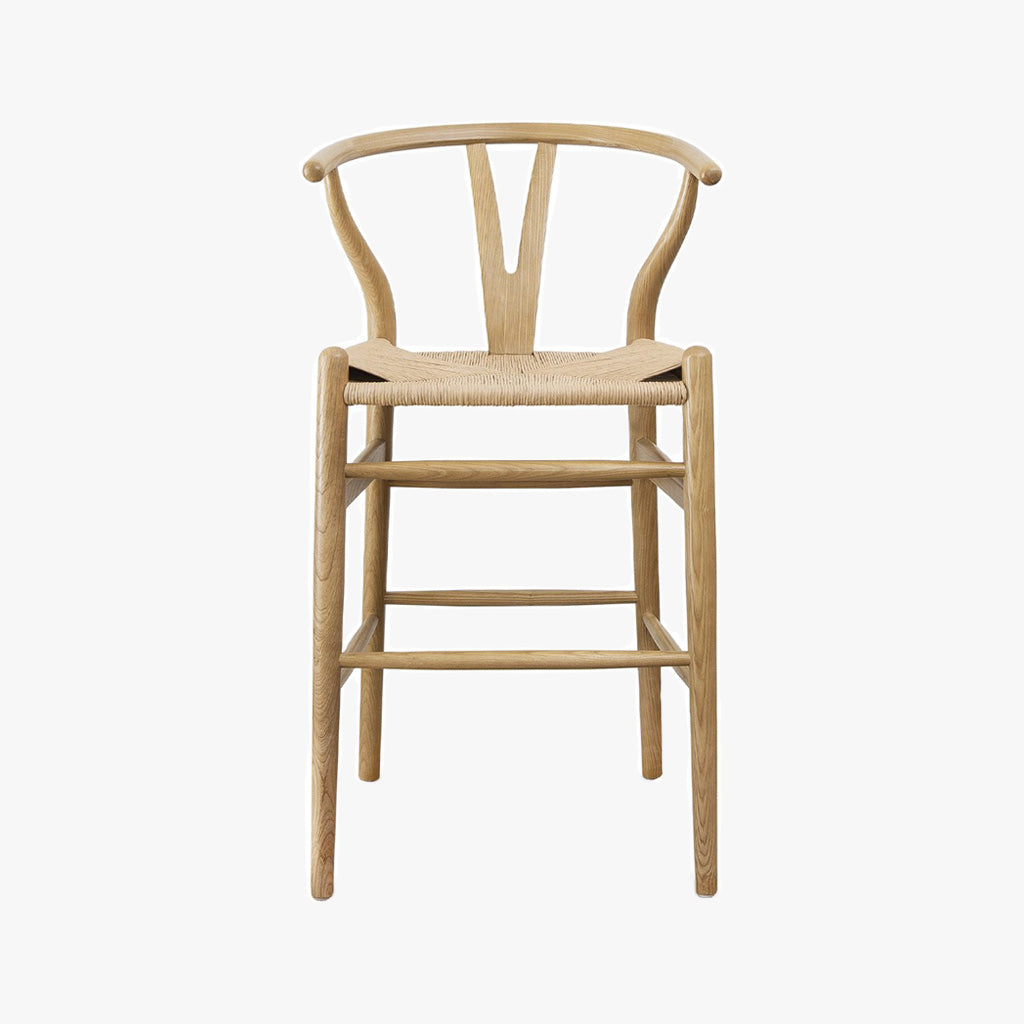 Front view of the Frida Counter Stool, blonde. A minimalist counter stool inspired by the mid-mod 1950s Hans J Wegner wishbone chairs with a Y-back design, curving top rail and tapered legs details.