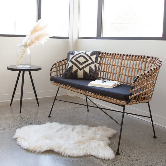 Calabria Bench shown in a corner of a room with a side table and large corner windows in the background.