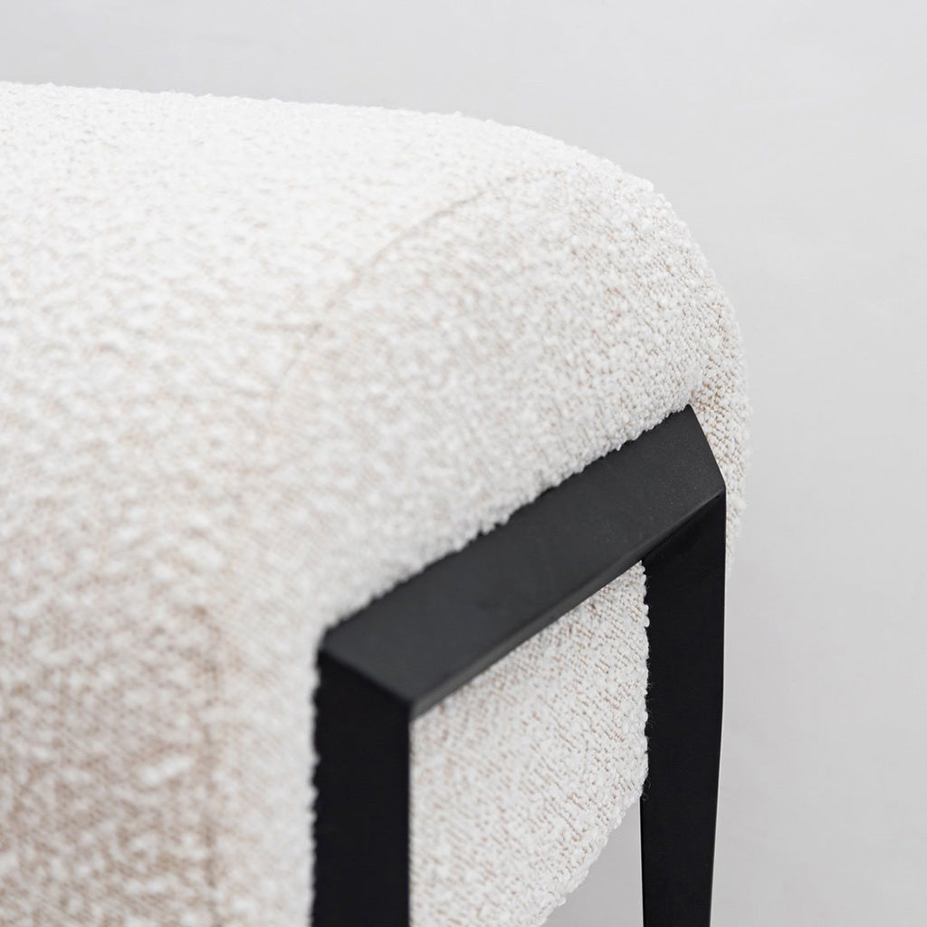 Closeup view of the Fisher Bench a minimal modern bench upholstered in an off-white boucle fabric with black metal legs.