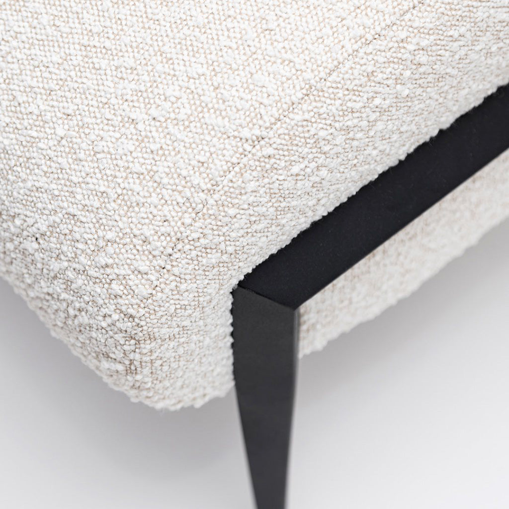 Closeup view of the Fisher Bench a minimal modern bench upholstered in an off-white boucle fabric with black metal legs.